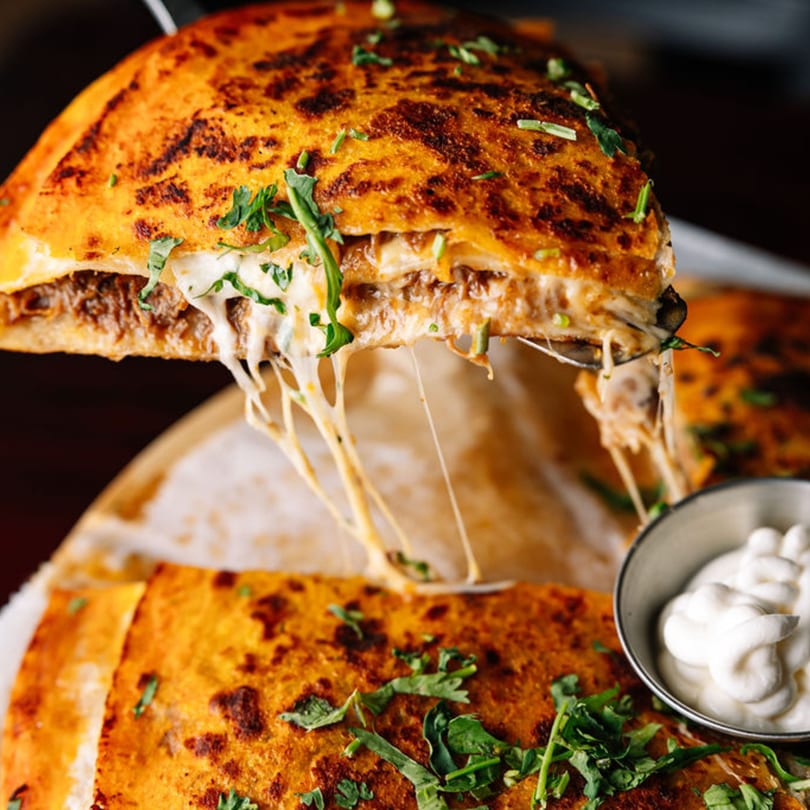 A cheesy quesadilla slice lifted, showing melted cheese pull, with a side of sour cream.