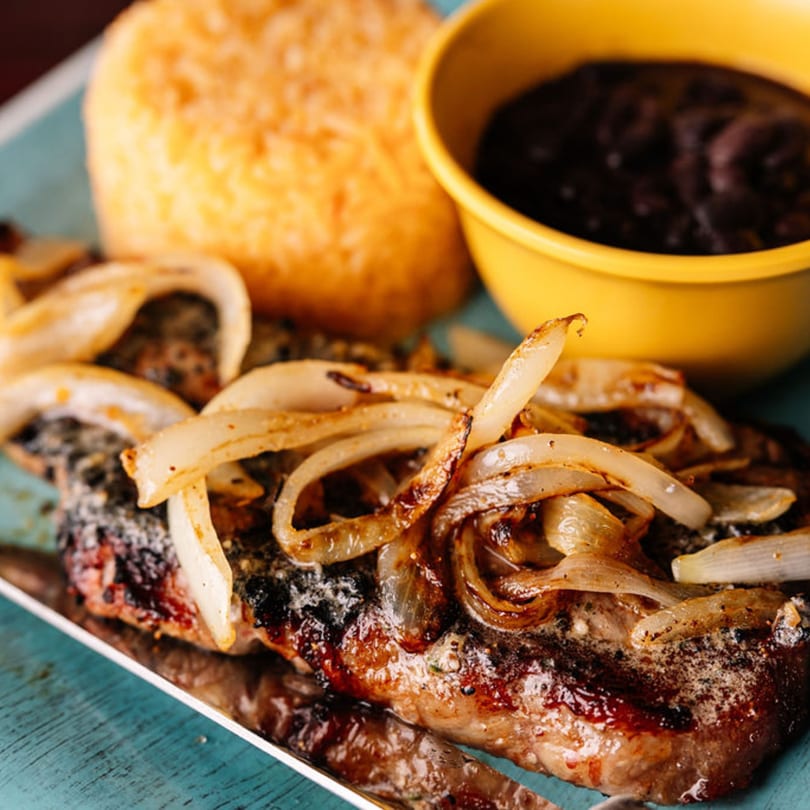Grilled steak topped with caramelized onions, served with yellow rice and black beans.