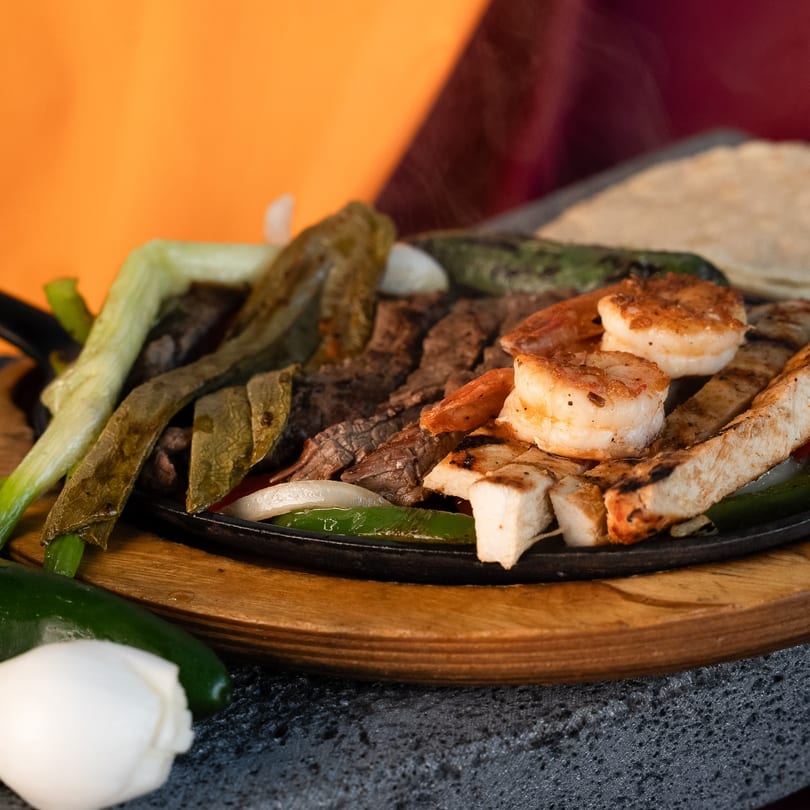 Sizzling fajitas with steak, chicken, shrimp, onions, and peppers on a cast iron skillet.