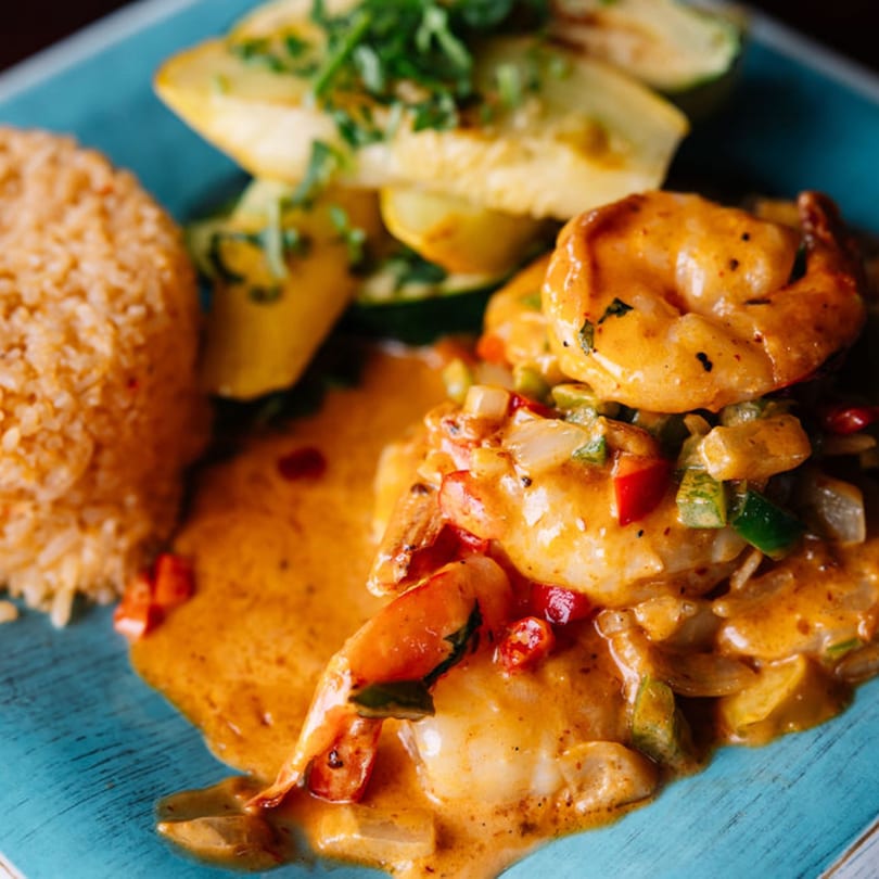 Shrimp in a creamy orange sauce with bell peppers, served with rice and sliced zucchini.