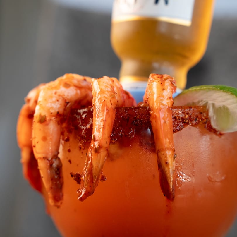 Shrimp cocktail with lime and a beer bottle in the background.