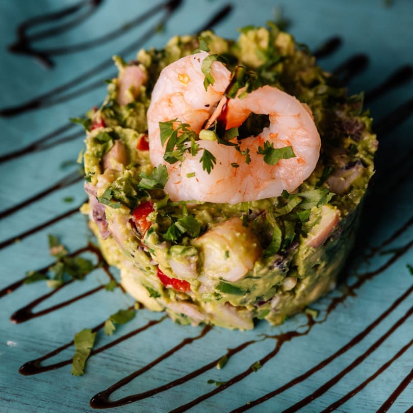 Guacamole topped with shrimp and cilantro, drizzled with balsamic glaze on a blue plate.